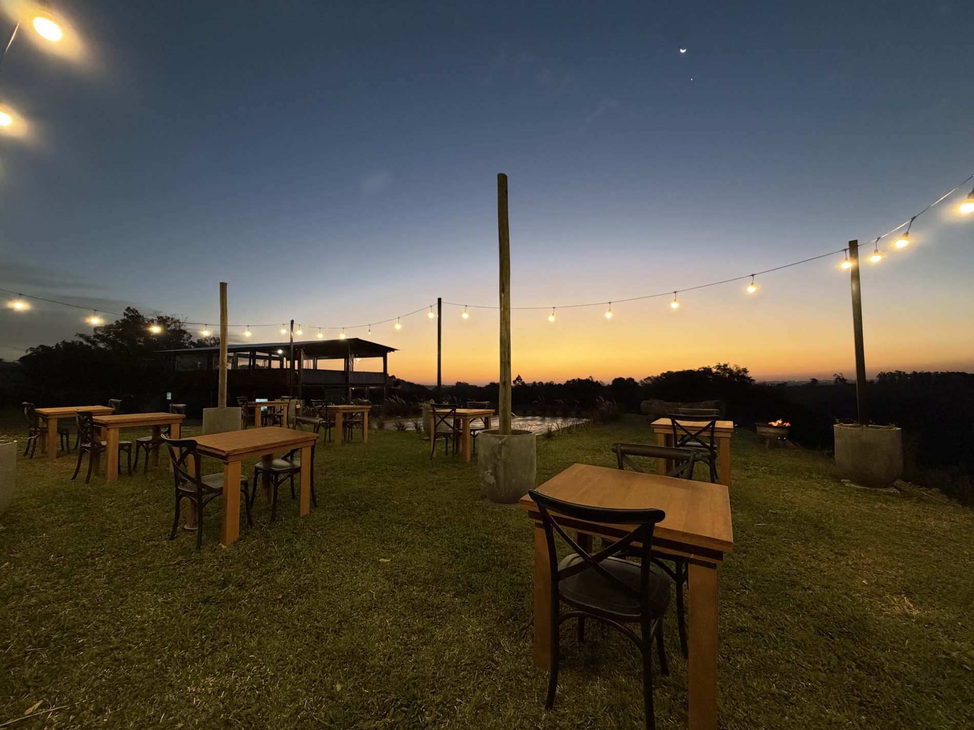 As mesas e o varal de luzes no fim da tarde, com o horizonte alaranjado